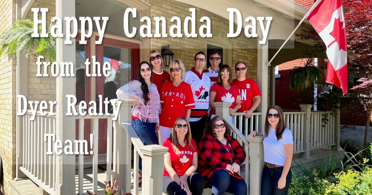 Team photo of the R.W. Dyer Realty Team-a group of people on a porch wearing red and white with a Canada Flag flying