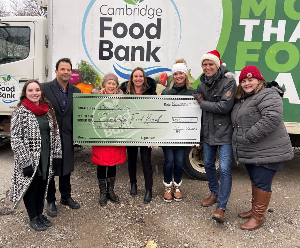 members of the R.W. Dyer Realty team pose with a giant cheque for $5,000 in front of the Cambridge Self-Help Food Bank Truck
